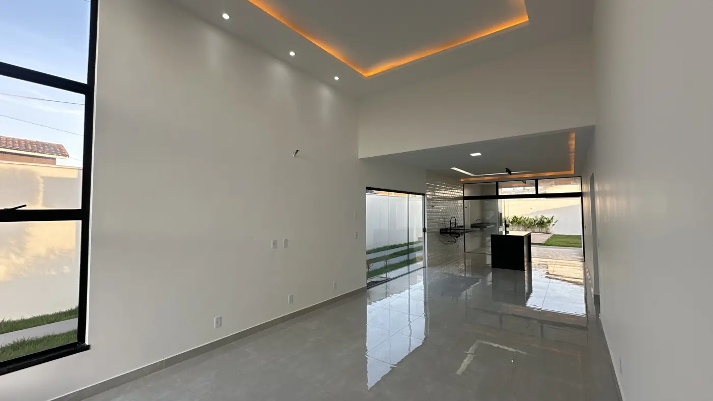 Sala com pé-direito alto e sanca iluminada, com a cozinha e a saída para o quintal ao fundo.