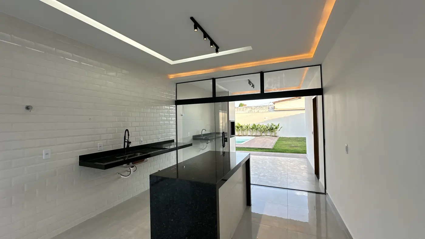 Cozinha americana com ilha central de pedra escura, parede de tijolinho branco e porta de vidro para o quintal.