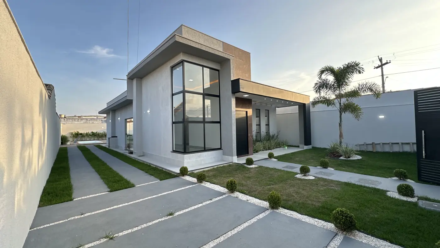 Fachada em ângulo, vista da calçada, com faixas de concreto entre a grama e o portão lateral.