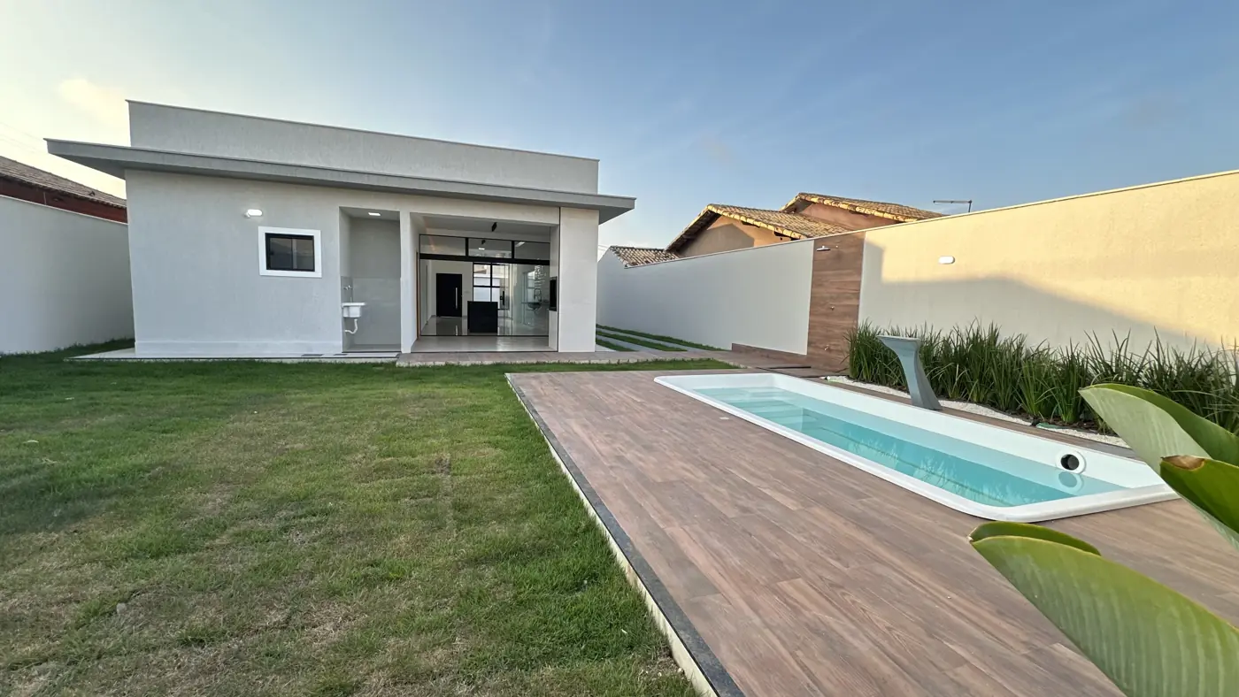 Casa vista do fundo do quintal gramado, com a área coberta dos fundos e a piscina em primeiro plano.
