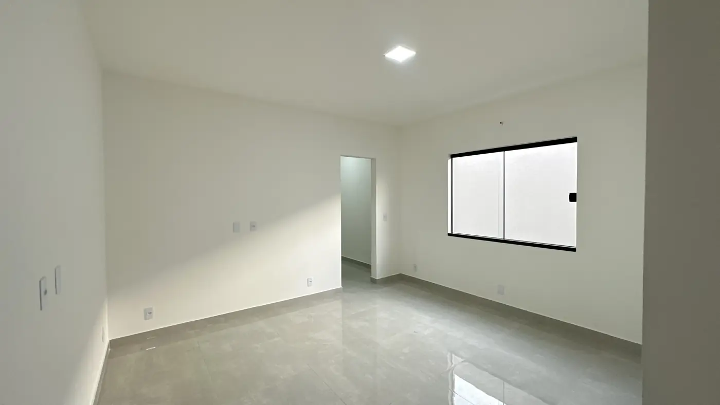 Quarto vazio com janela de correr e uma passagem aberta para o cômodo ao lado.