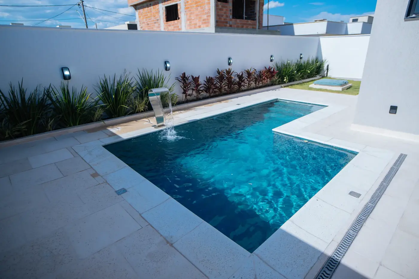 Piscina em nível com o piso da área externa, junto ao muro do lote.