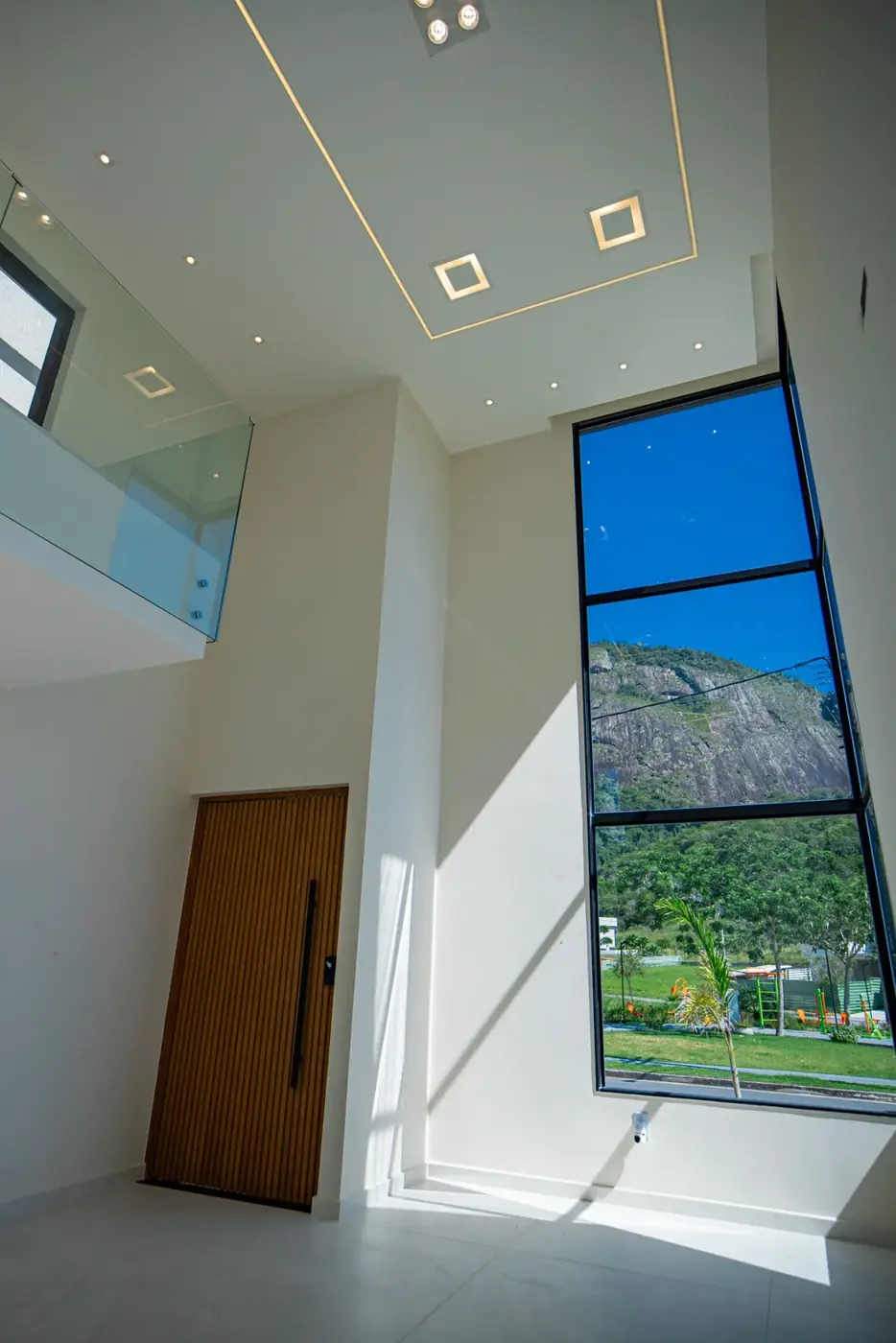 Sala de pé-direito duplo, com escada e esquadria alta de vidro.