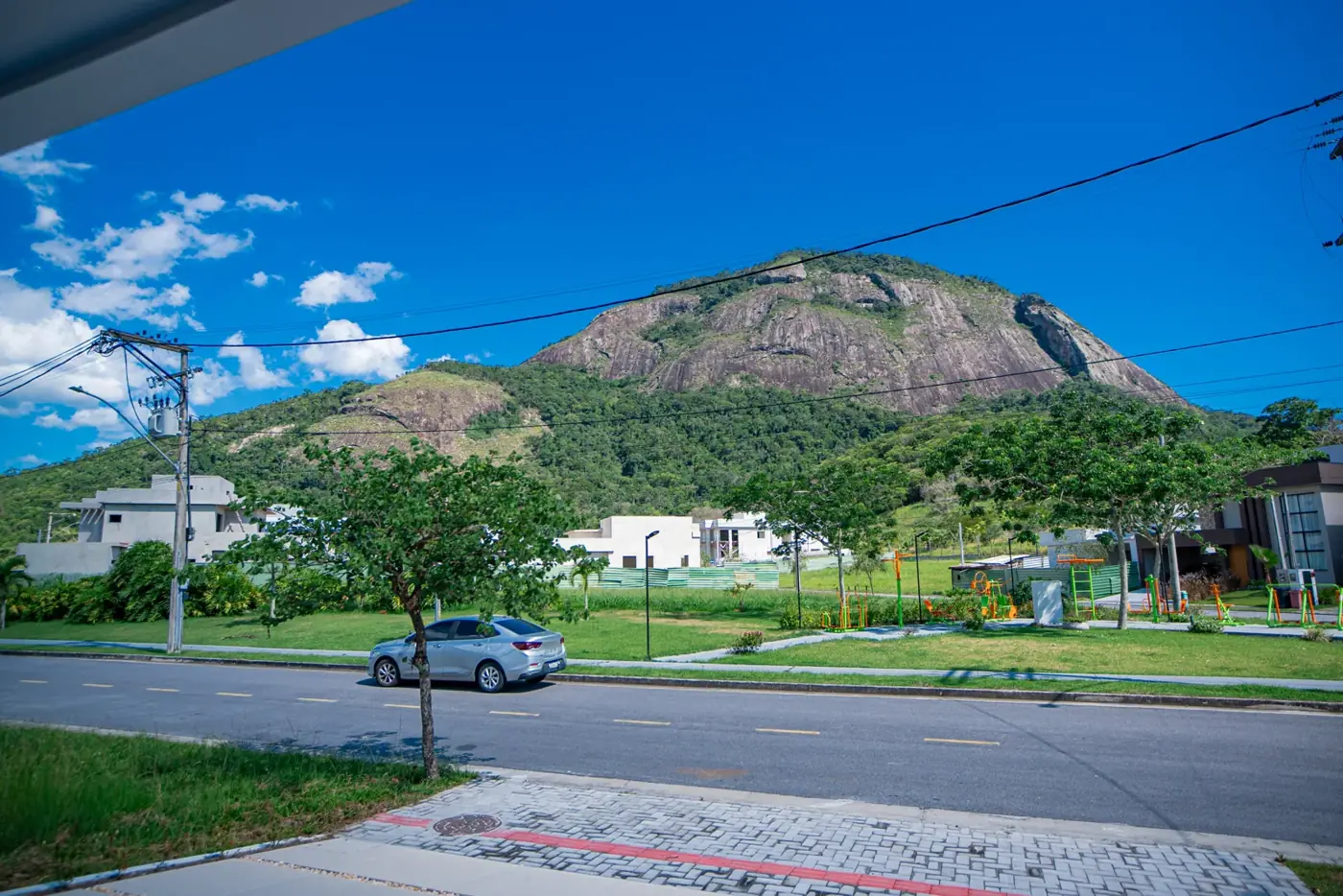 Frente da casa vista da rua do condomínio, com o morro de pedra ao fundo.