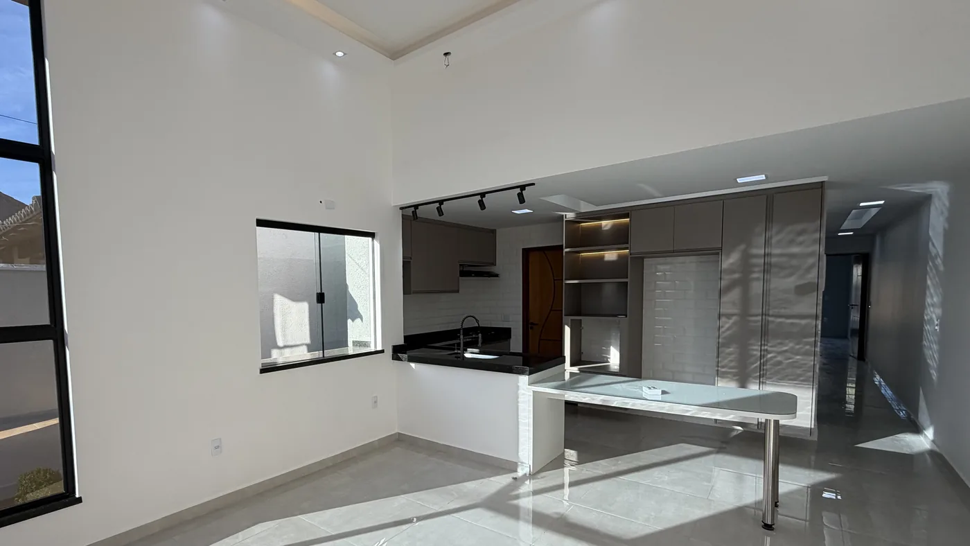 Sala de pé-direito alto com sanca iluminada, esquadria preta à esquerda e a cozinha planejada integrada ao fundo.