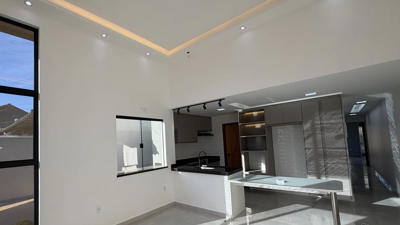 Sala e cozinha integradas na mesma enfiada, com esquadria preta alta, piso claro polido e bancada ao fundo.