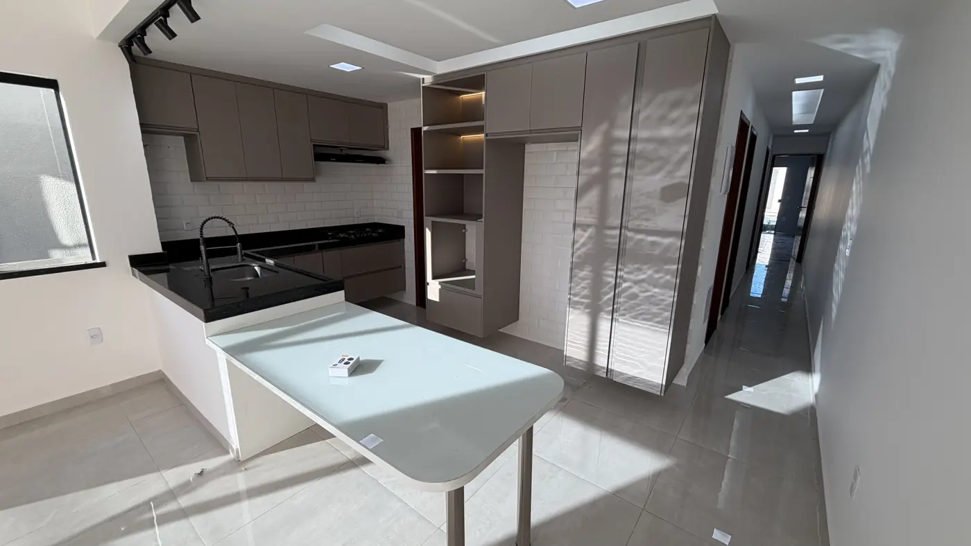 Cozinha com armários planejados, bancada escura com cuba, torneira preta e mesa planejada de tampo claro.