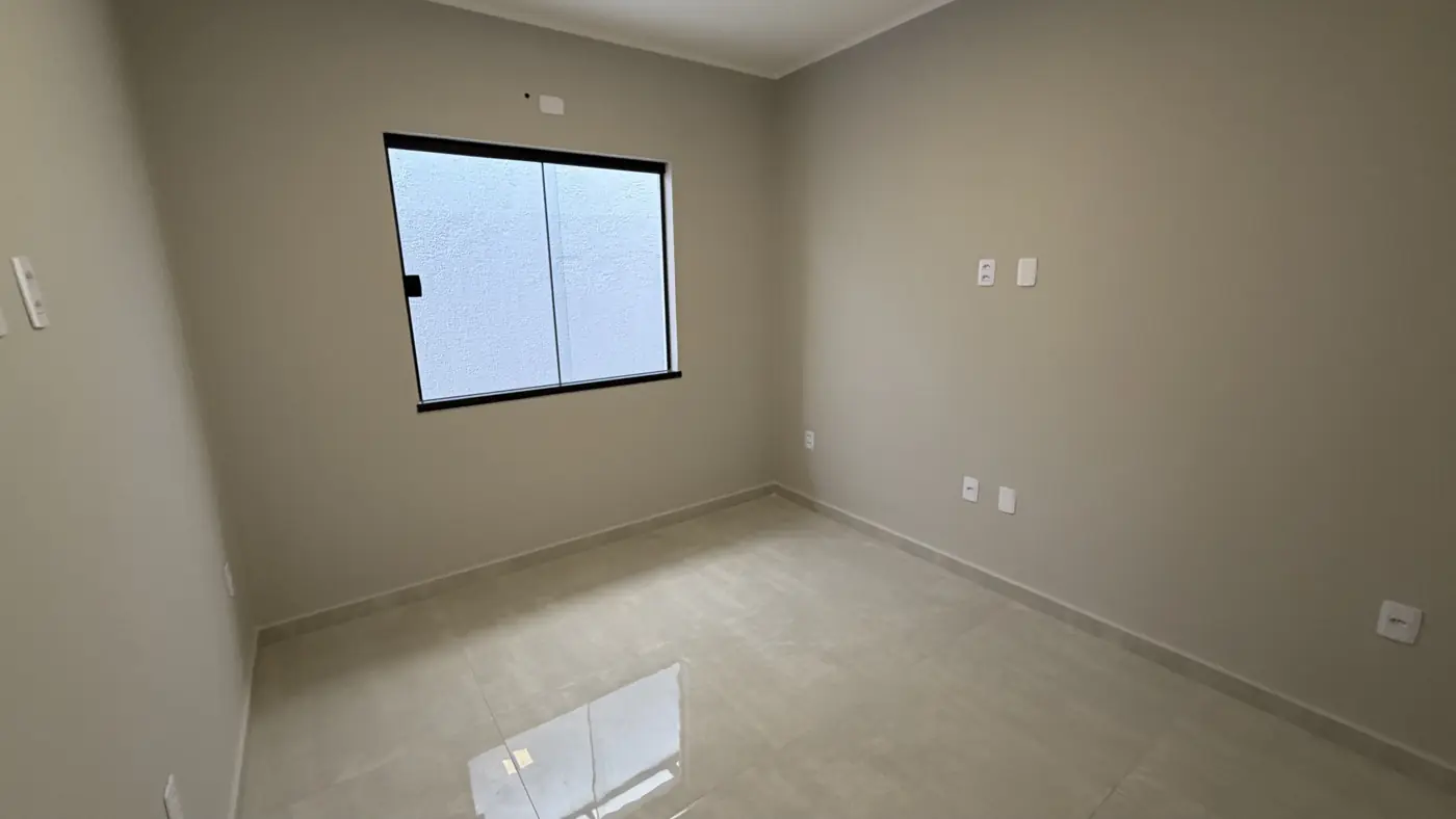 Quarto vazio com janela de correr de esquadria preta, paredes claras e piso claro polido.