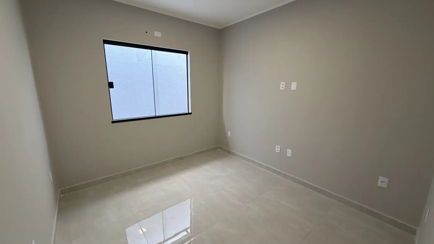 Outro quarto vazio, com janela de correr de esquadria preta e piso claro polido.