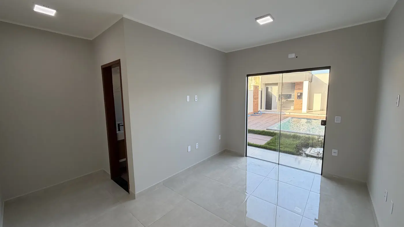 Quarto com porta de madeira e porta de vidro de correr dando para o quintal, com a grama e a piscina visíveis lá fora.